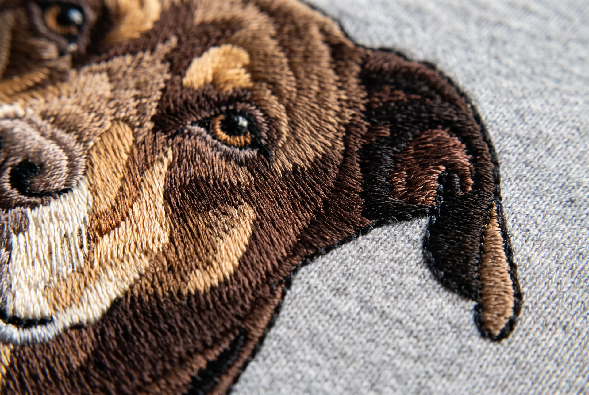 Macro photograph of an embroidered dog portrait showing individual satin stitches and thread sheen